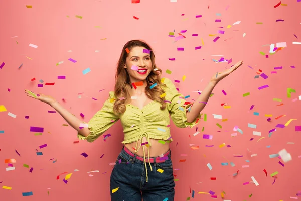 Happy woman with outstretched hands near confetti on pink — Stock Photo