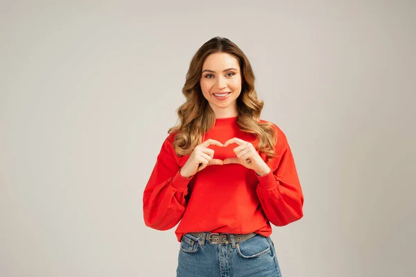 Mujer feliz mostrando el signo del corazón con las manos aisladas en gris - foto de stock