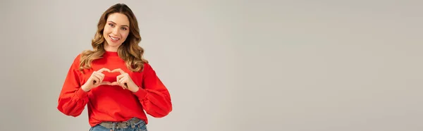 Femme heureuse montrant signe du coeur avec les mains isolées sur gris, bannière — Photo de stock