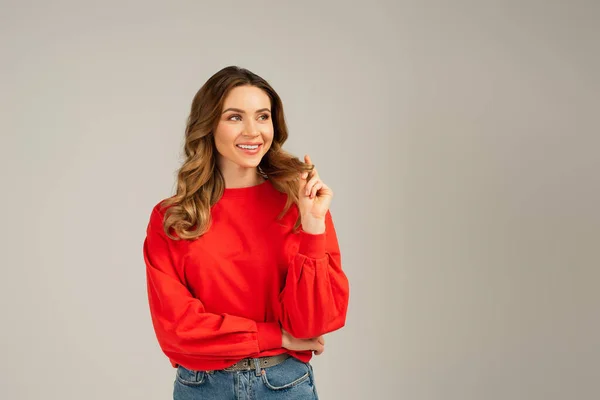 Mulher encaracolado tocando o cabelo enquanto sorrindo isolado no cinza — Fotografia de Stock