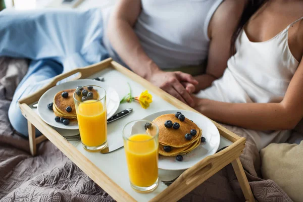 Breakfast tray with pancakes and orange juice near couple in bed — Stock Photo