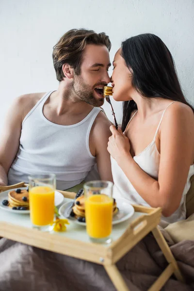 Happy couple eating pancakes from same fork in bed — Stock Photo