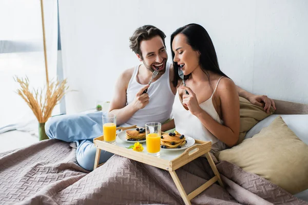 Радостная пара с вкусным завтраком в постели — стоковое фото