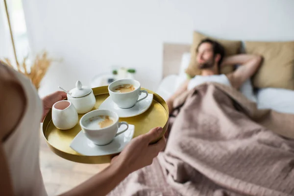 Woman holding tray with cups of coffee near blurred and sleeping man — Stock Photo