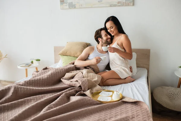Happy couple holding cups of coffee in bed — Stock Photo
