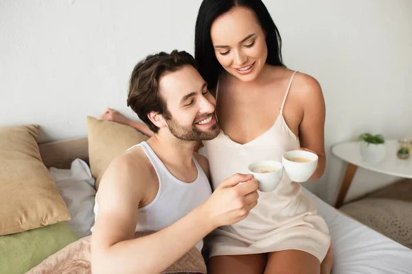 Casal feliz copos clinking de cappuccino na cama — Fotografia de Stock