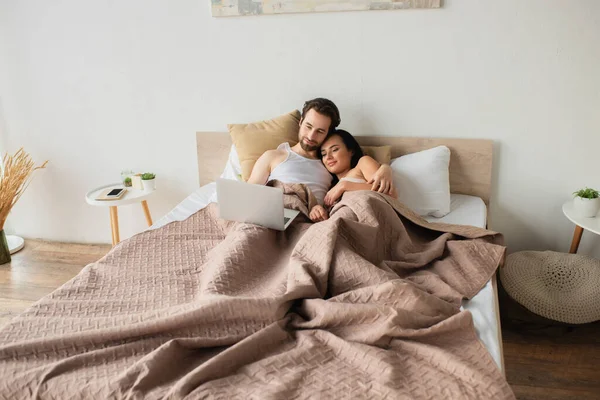 Feliz pareja acostada en la cama y viendo la película en el ordenador portátil - foto de stock