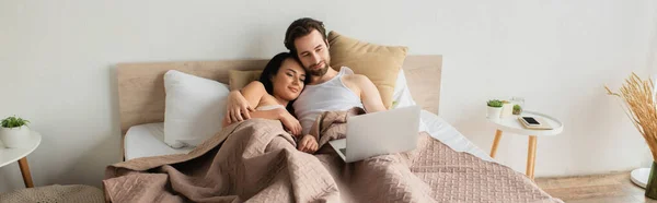 Feliz pareja acostada en la cama y viendo la película en el ordenador portátil, bandera - foto de stock