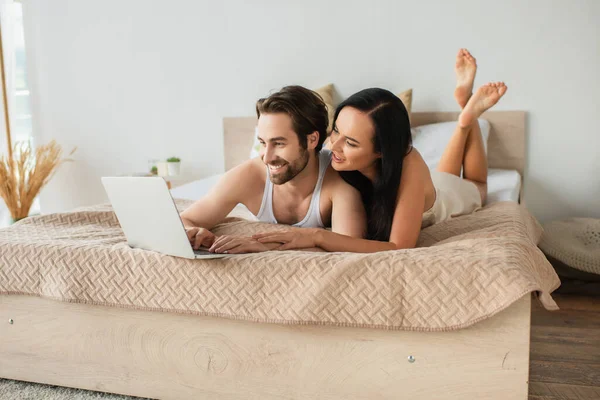 Feliz pareja viendo la película en el ordenador portátil mientras está acostado en la cama - foto de stock