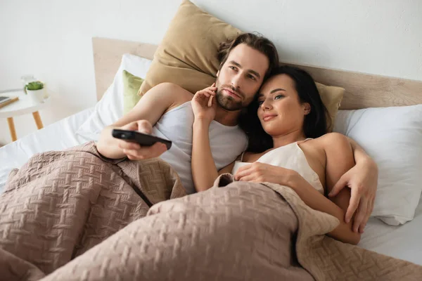 Молодая пара лежит в постели и смотрит телевизор — стоковое фото