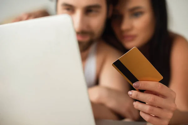 Pareja borrosa celebración de la tarjeta de crédito cerca del ordenador portátil, mientras que las compras en línea - foto de stock
