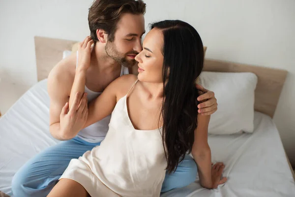 Homem barbudo abraçando namorada feliz em camisola vestido na cama — Fotografia de Stock