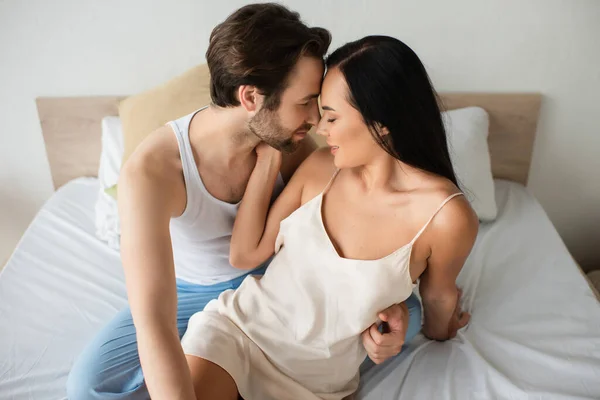 Barbudo hombre abrazando alegre novia en camisola vestido en la cama - foto de stock