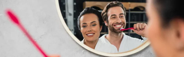 Reflexión en el espejo de la feliz pareja joven en batas blancas cepillarse los dientes, bandera - foto de stock