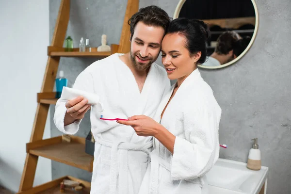 Glücklicher Mann drückt Zahnpasta auf Zahnbürste seiner Freundin — Stockfoto