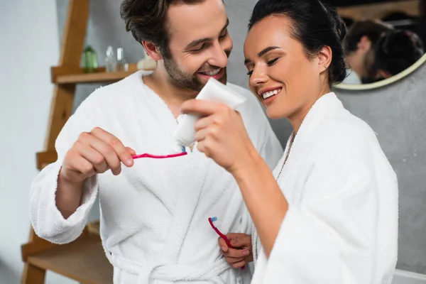 Glückliche Frau drückt Zahnpasta auf Zahnbürste ihres Freundes — Stockfoto