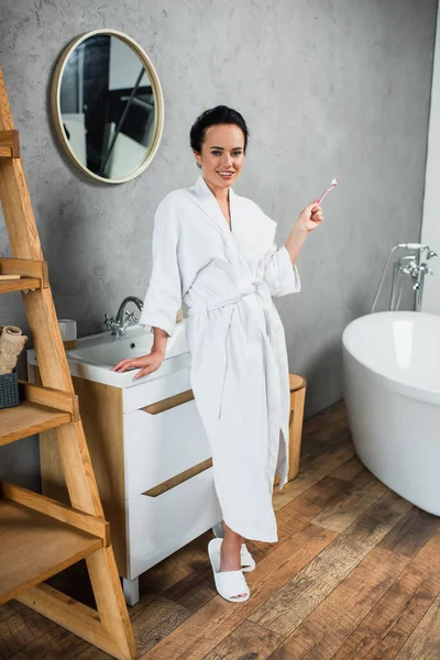 Полная длина счастливой женщины, держащей зубную щетку в современной ванной комнате — стоковое фото