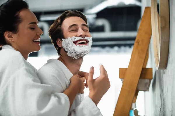 Femme heureuse étreignant petit ami avec mousse à raser sur le visage — Photo de stock