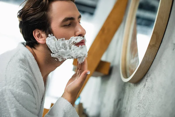 Man applying shaving cream on face near mirror — Stock Photo