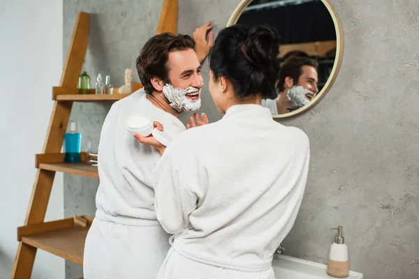 Femme regardant homme heureux avec mousse à raser sur le visage — Photo de stock