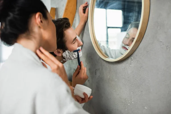 Homme rasage près floue copine dans salle de bain — Photo de stock