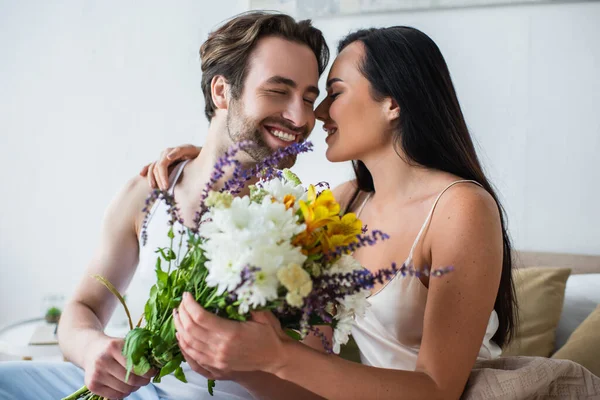 Glücklicher Mann übergibt Blumenstrauß an lächelnde Freundin im Schlafzimmer — Stockfoto