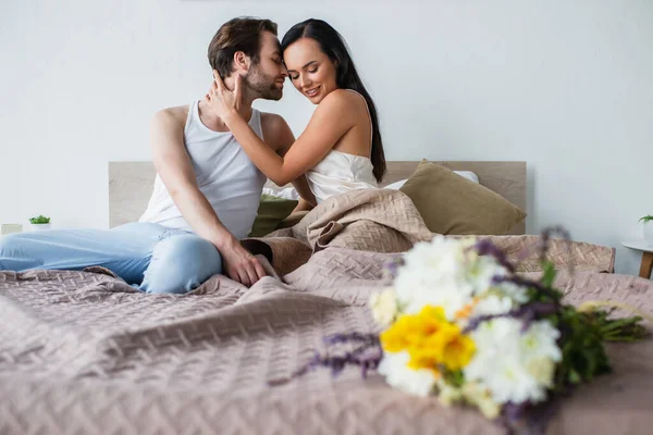 Verschwommener Blumenstrauß in der Nähe eines glücklichen Paares, das sich im Bett umarmt — Stockfoto