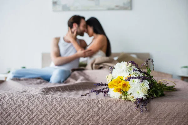 Buquê de flores perto de casal borrado abraçando na cama — Fotografia de Stock