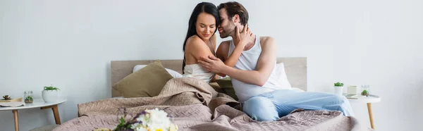 Zufriedenes Paar, das sich neben Blumenstrauß auf dem Bett umarmt, Banner — Stockfoto