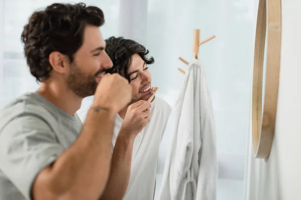 Feliz gay pareja cepillado dientes cerca espejo en cuarto de baño - foto de stock