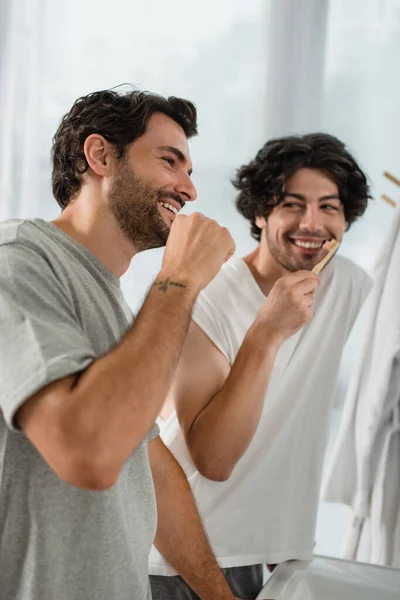 Позитивная пара геев чистят зубы в ванной комнате — стоковое фото