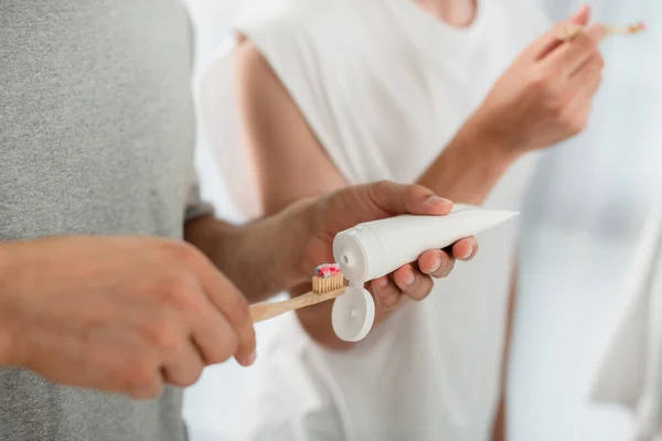 Cropped view of man squeezing toothpaste on toothbrush near boyfriend in bathroom — Stock Photo