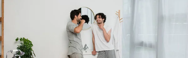 Bearded gay couple looking at each other and smiling while brushing teeth in morning, banner — Stock Photo