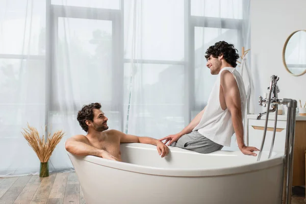 Feliz gay hombre mirando novio en bañera - foto de stock