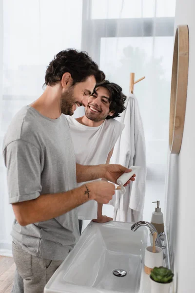 Glücklich homosexuell mann looking at boyfriend squeezing zahnpasta im badezimmer — Stockfoto