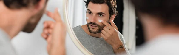 Homme tatoué appliquer de la crème sur le visage près de petit ami flou, bannière — Photo de stock