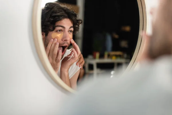 Homosexual hombre aplicando parches en los ojos y mirando el espejo - foto de stock