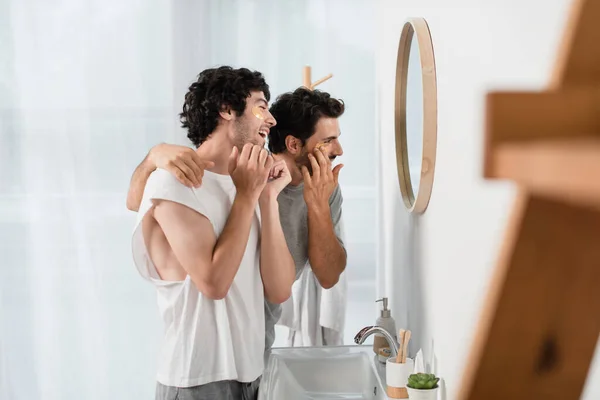 Glückliches homosexuelles Paar, das Augenklappen im Badezimmer aufträgt — Stockfoto