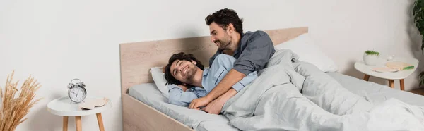 Щаслива гей пара в піжамах обіймається, лежачи на ліжку, банер — стокове фото