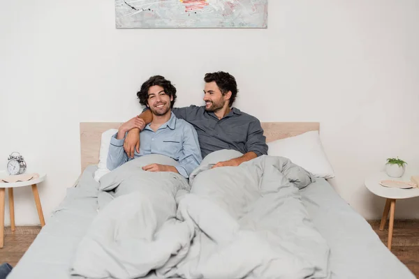 Joyeux gay couple souriant tout en refroidissant dans lit — Photo de stock