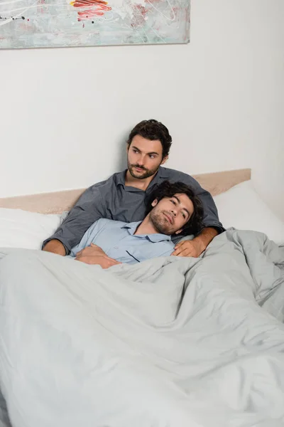 Gay hombre apoyándose en novio en cama - foto de stock