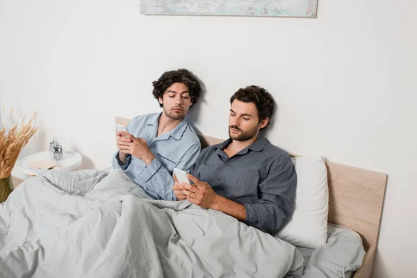 Hombre mirando el teléfono móvil mientras novio mensajes de texto en la cama - foto de stock
