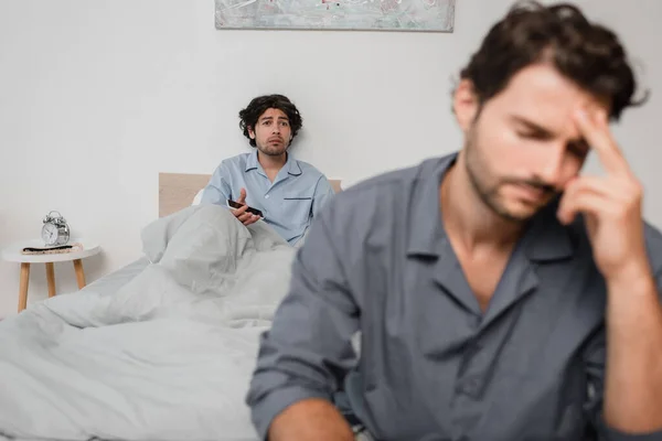 Hombre molesto sosteniendo teléfono inteligente y mirando novio cansado en primer plano borrosa - foto de stock