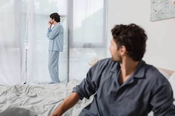 Mann steht und schaut Fenster an, mit verschwommenem Freund im Vordergrund, Konzept der Beziehungsschwierigkeiten — Stockfoto