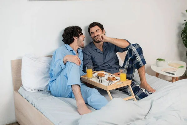 Alegre gay pareja mirando uno a otro cerca bandeja con desayuno - foto de stock