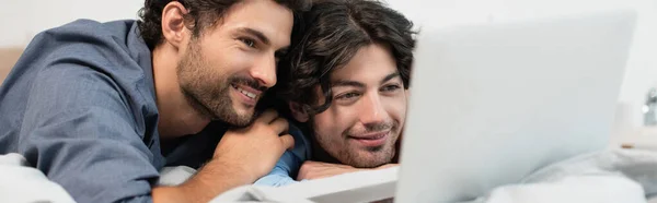 Felice coppia gay guardando film su laptop in camera da letto, banner — Foto stock