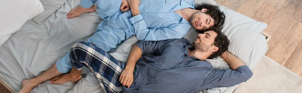 Vista superior de feliz pareja gay en pijama descansando en la cama, pancarta - foto de stock