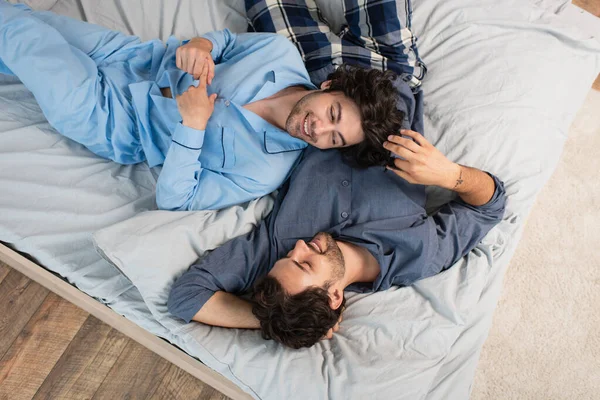 Blick von oben auf fröhliches homosexuelles Paar im Schlafanzug, das auf dem Bett ruht — Stockfoto