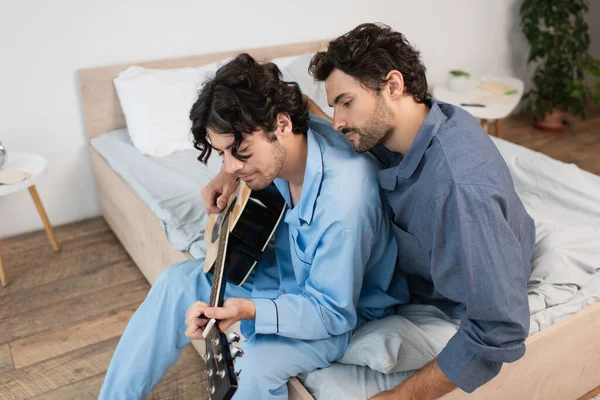 Schwuler Mann spielt Akustikgitarre in der Nähe eines bärtigen Freundes im Bett — Stockfoto