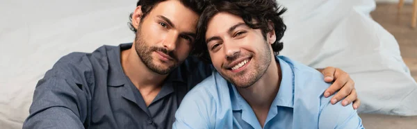 Cheerful young gay couple hugging in bedroom, banner — Stock Photo